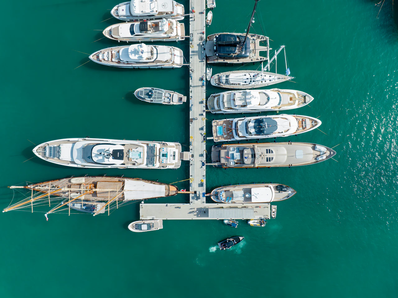 Aerial view of multiple superyachts moored at a marina pier in turquoise water.