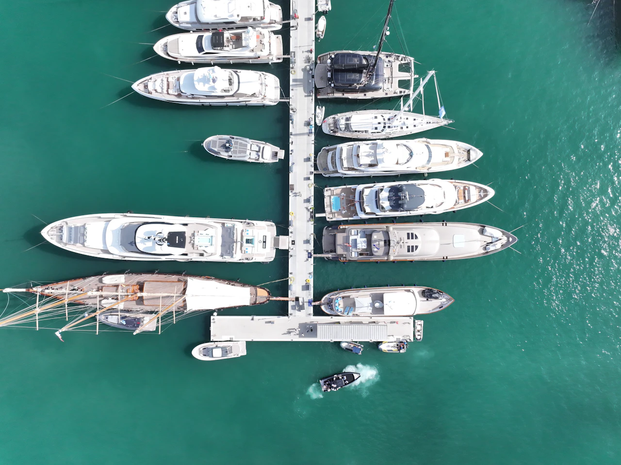 Aerial view of multiple superyachts moored at a marina dock in turquoise water.