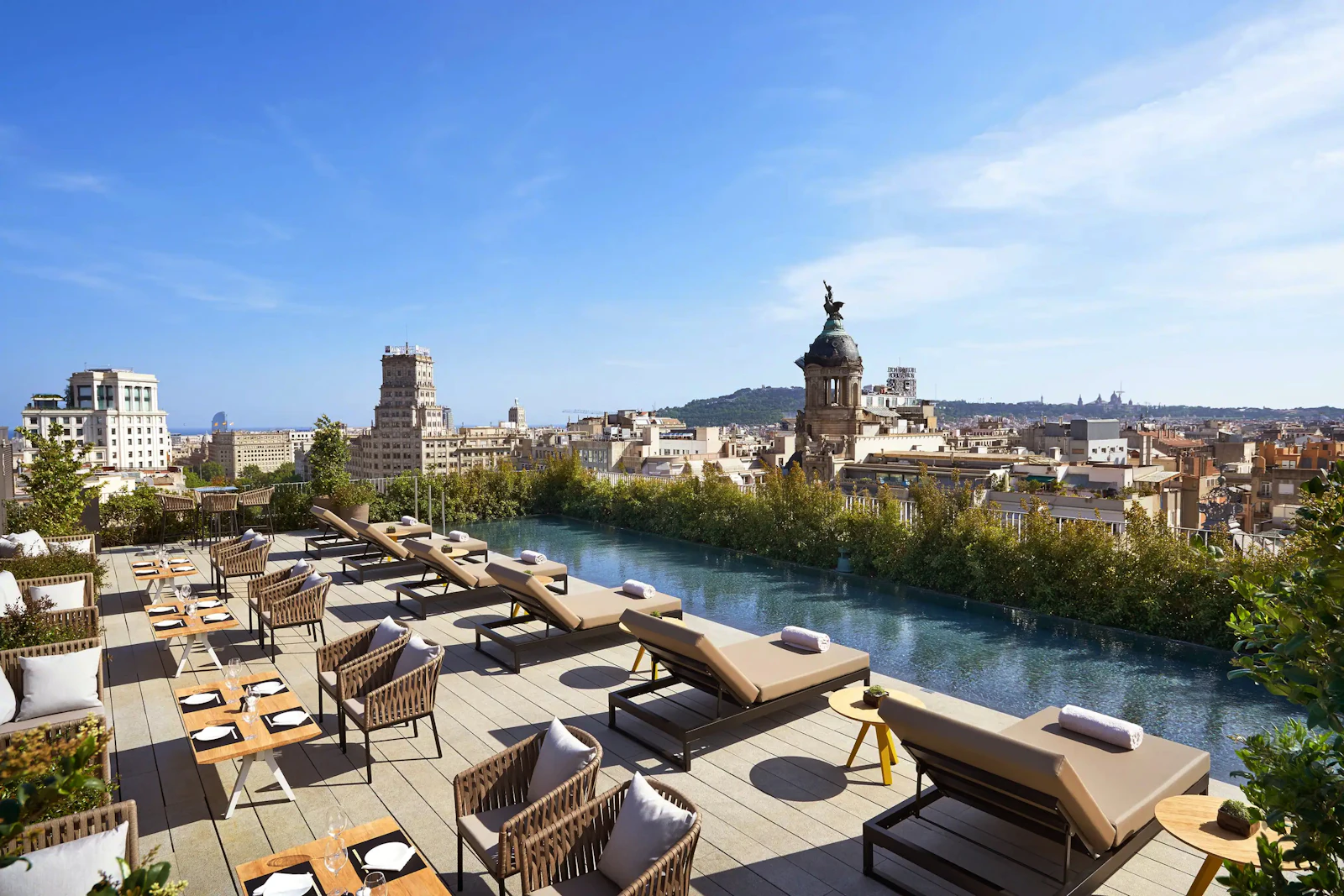 Rooftop terrace with loungers, dining tables and a pool overlooking the Barcelona skyline.