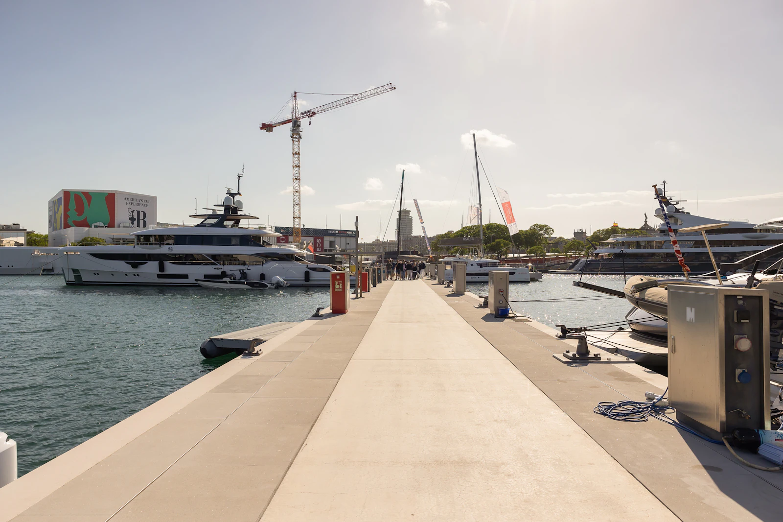 A marina dock lined with moored yachts, with a construction crane in the background.