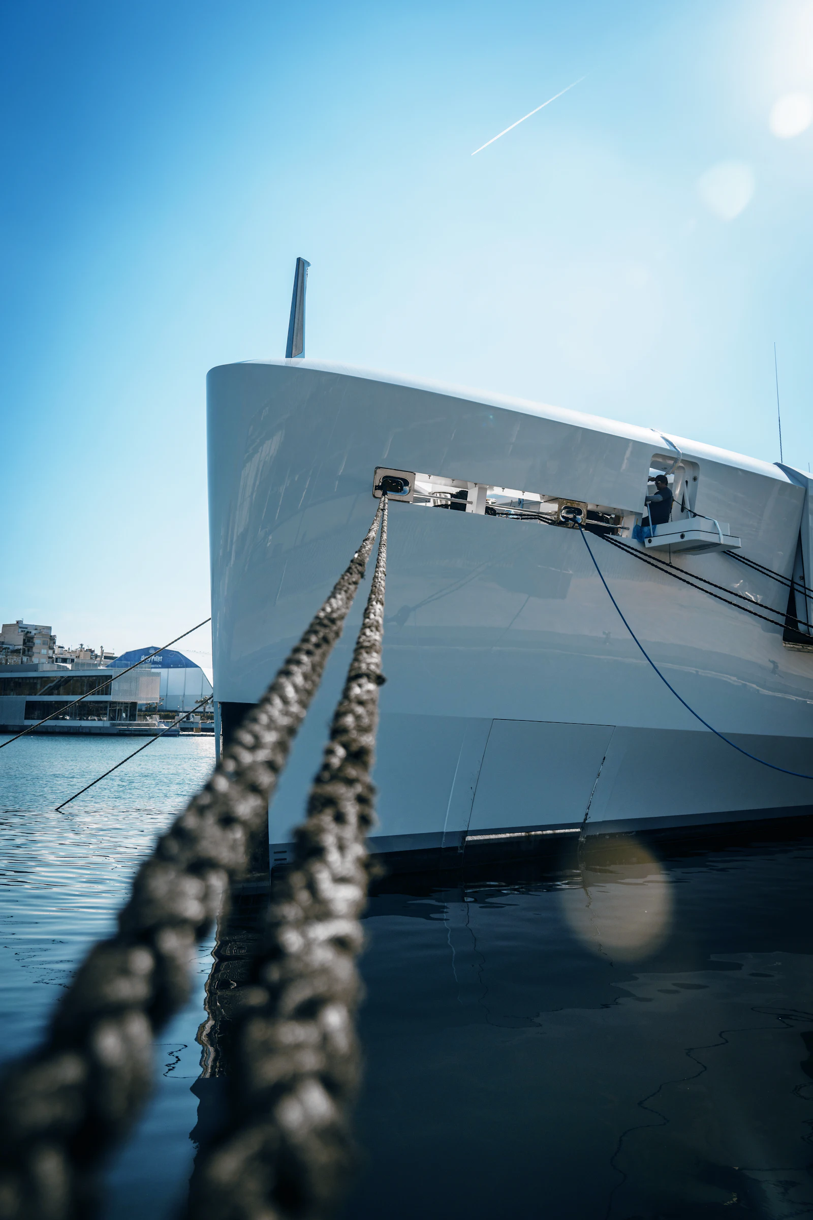 Large superyacht moored at marina with rope in foreground and clear blue sky.