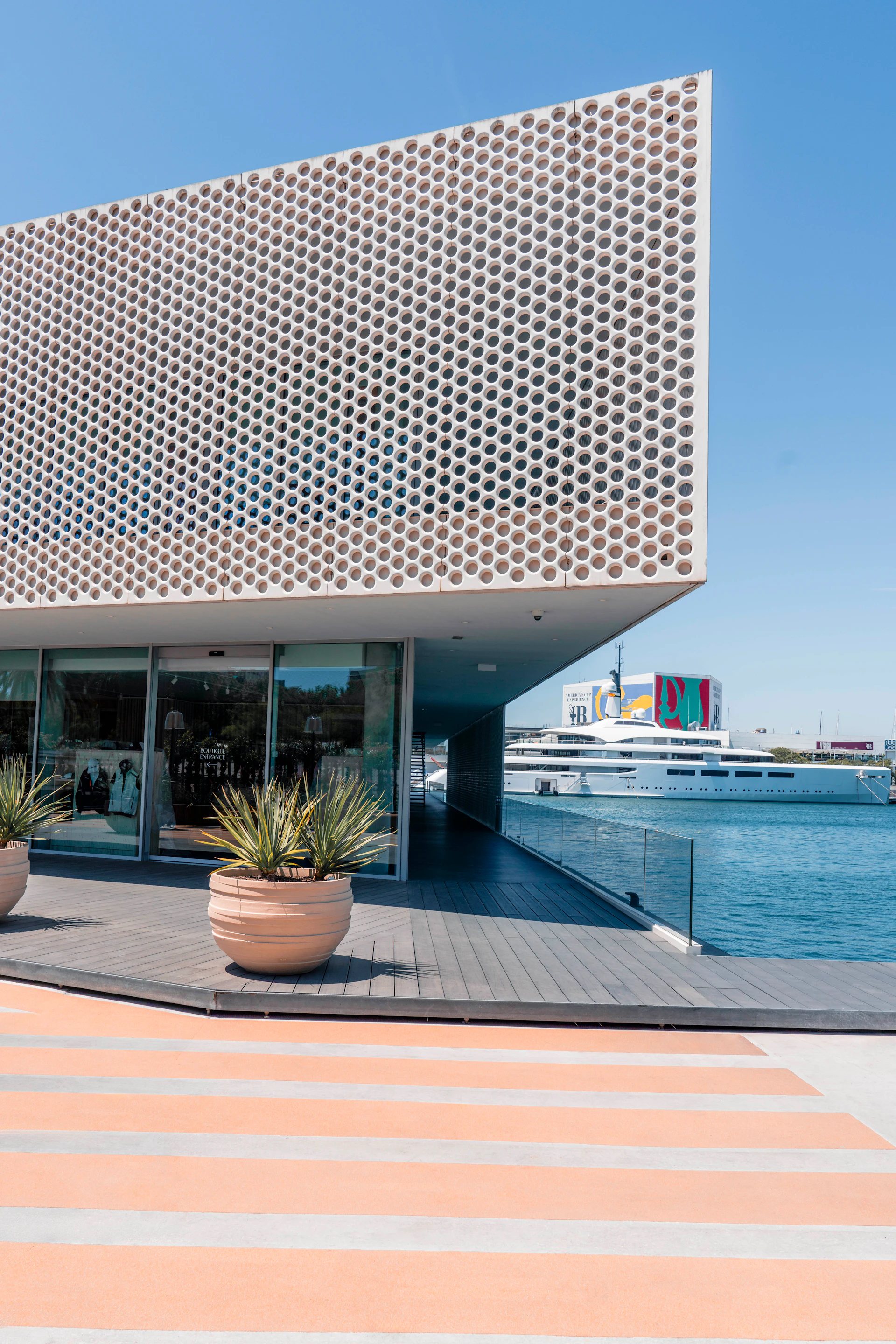 Modern waterfront building with perforated facade overlooking superyachts docked at marina.