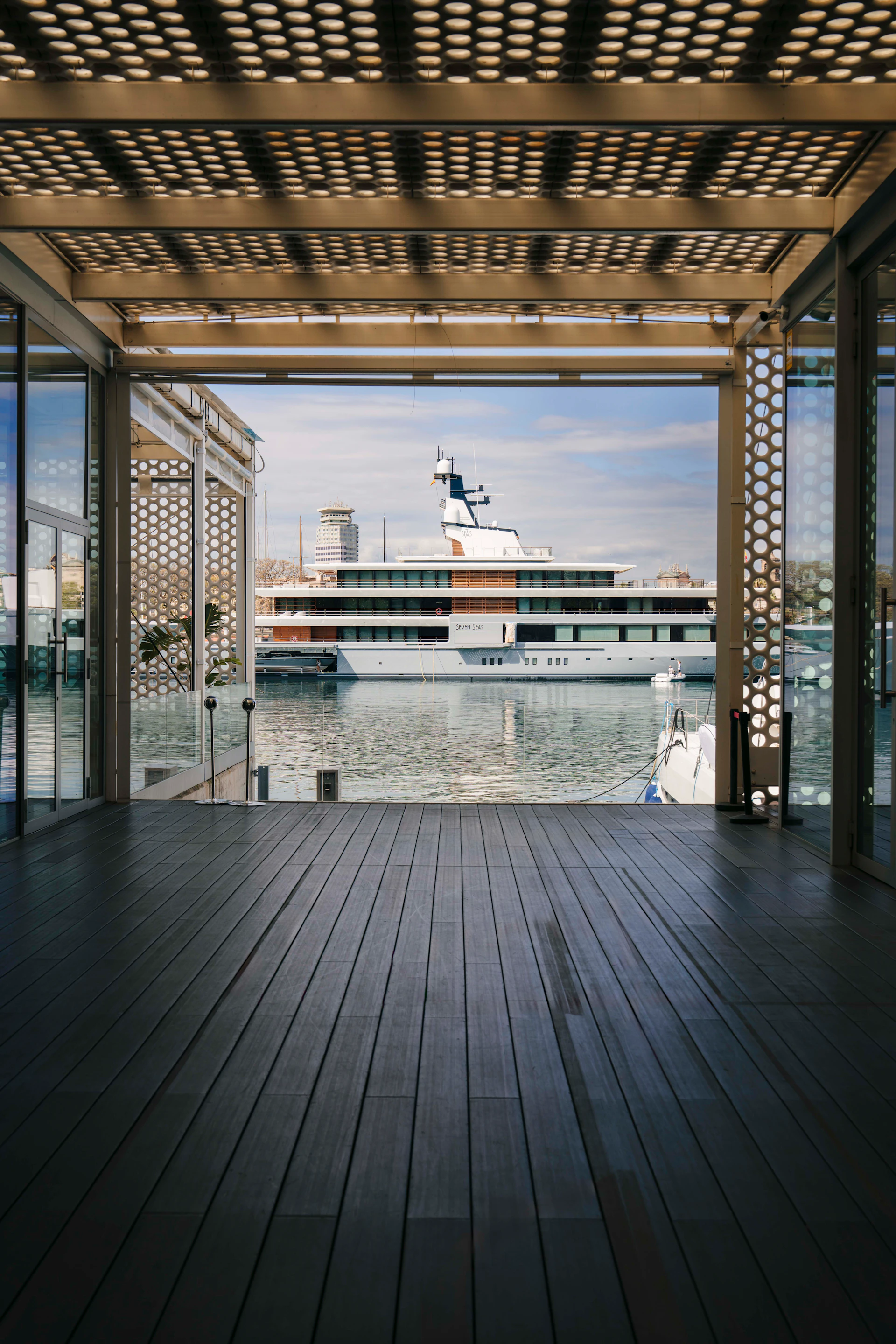 View from a modern waterfront terrace looking out at a large superyacht moored in the marina.