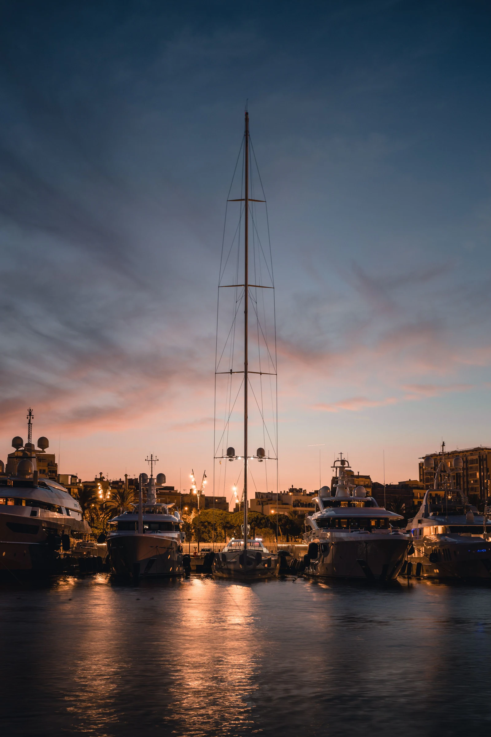 Superyachts moored in Barcelona marina with city skyline and blue sky in background.