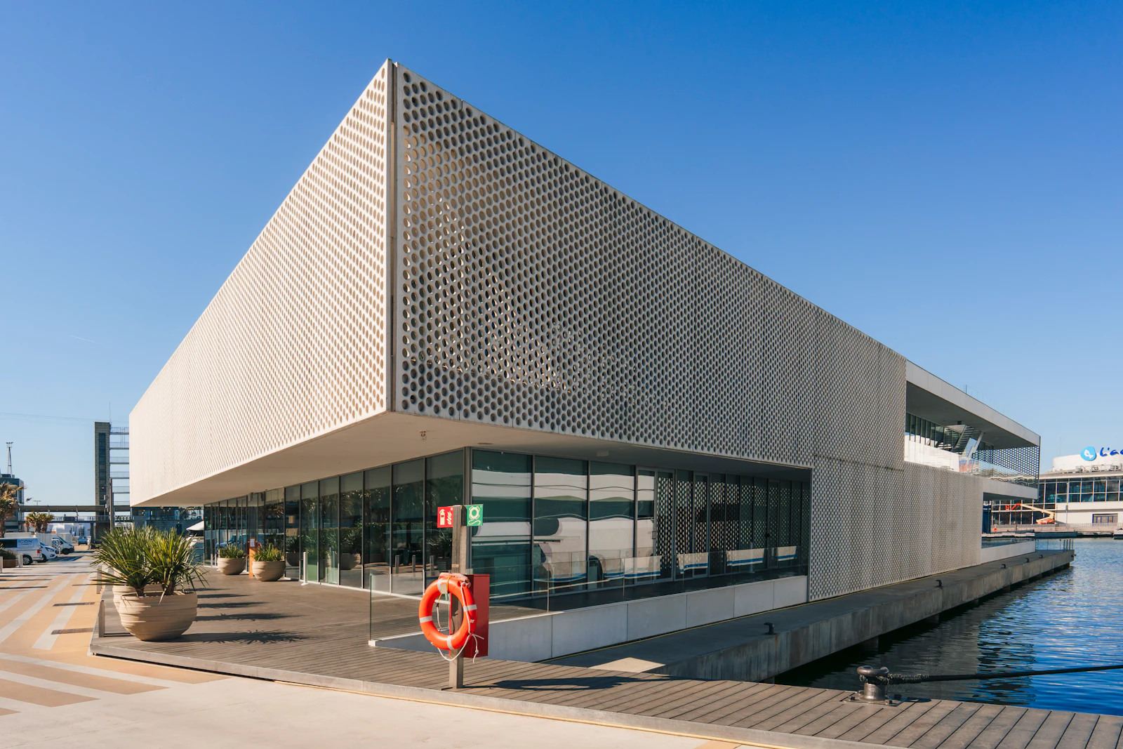 Modern waterfront building with perforated metal facade beside a wooden dock and blue water.
