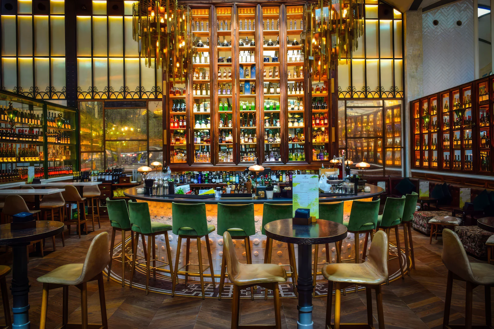 Elegant bar with green velvet stools and tall shelves of bottles.