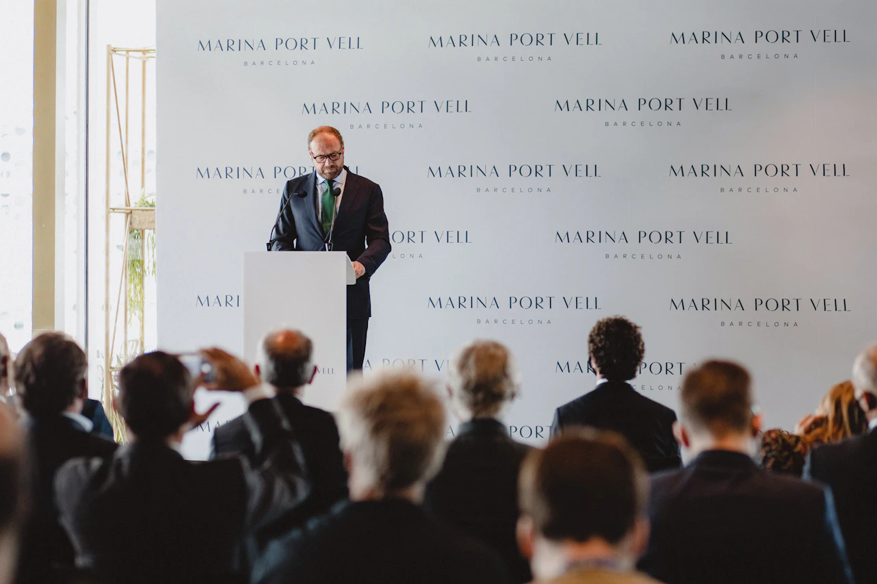 Man in business suit speaking at podium during Marina Port Vell Barcelona event.