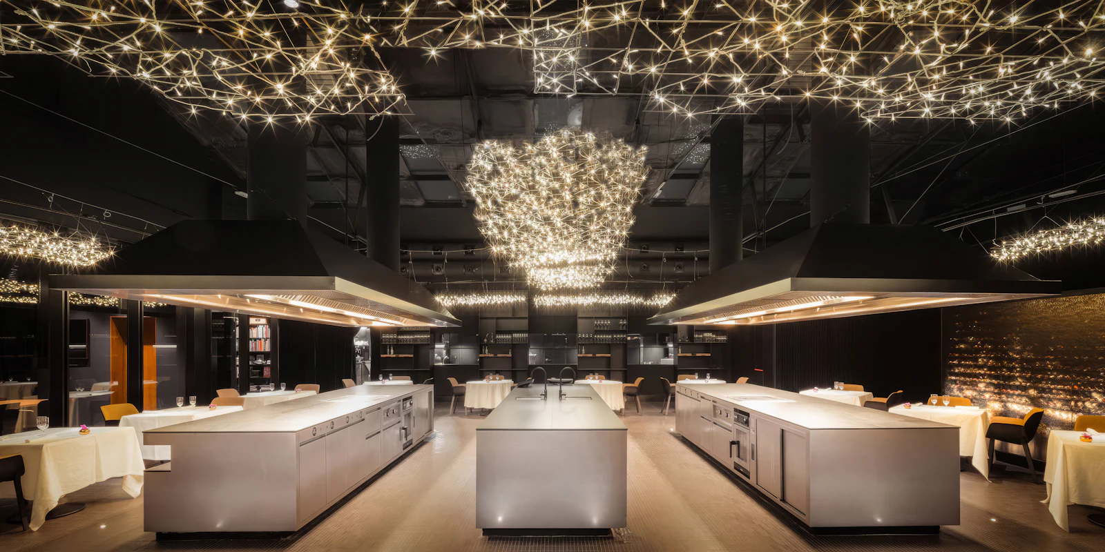 Modern restaurant with open stainless steel kitchen islands and sparkling star-like ceiling lights.