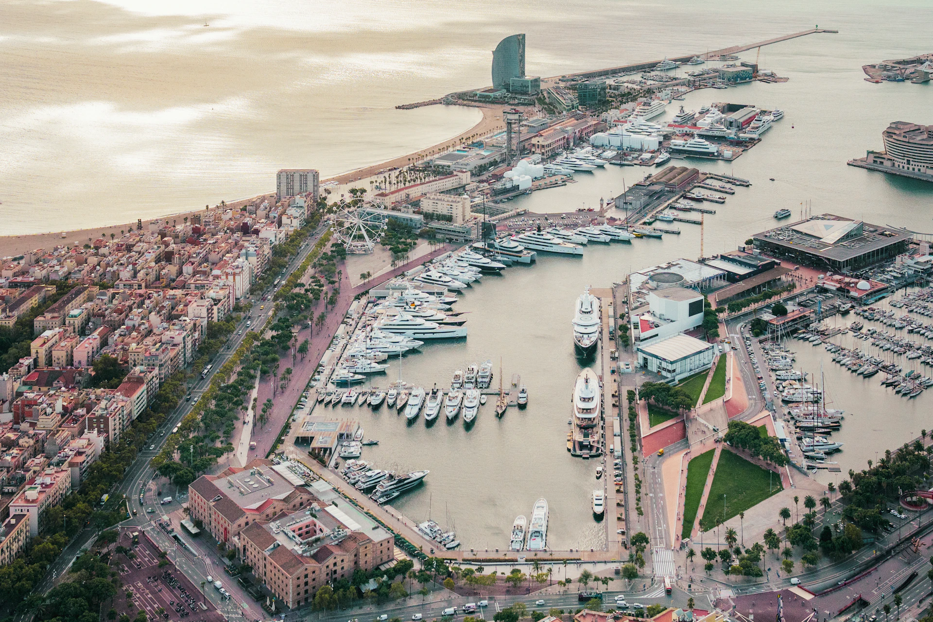 Aerial view of Marina Port Vell with moored superyachts, Barcelona waterfront and city buildings.