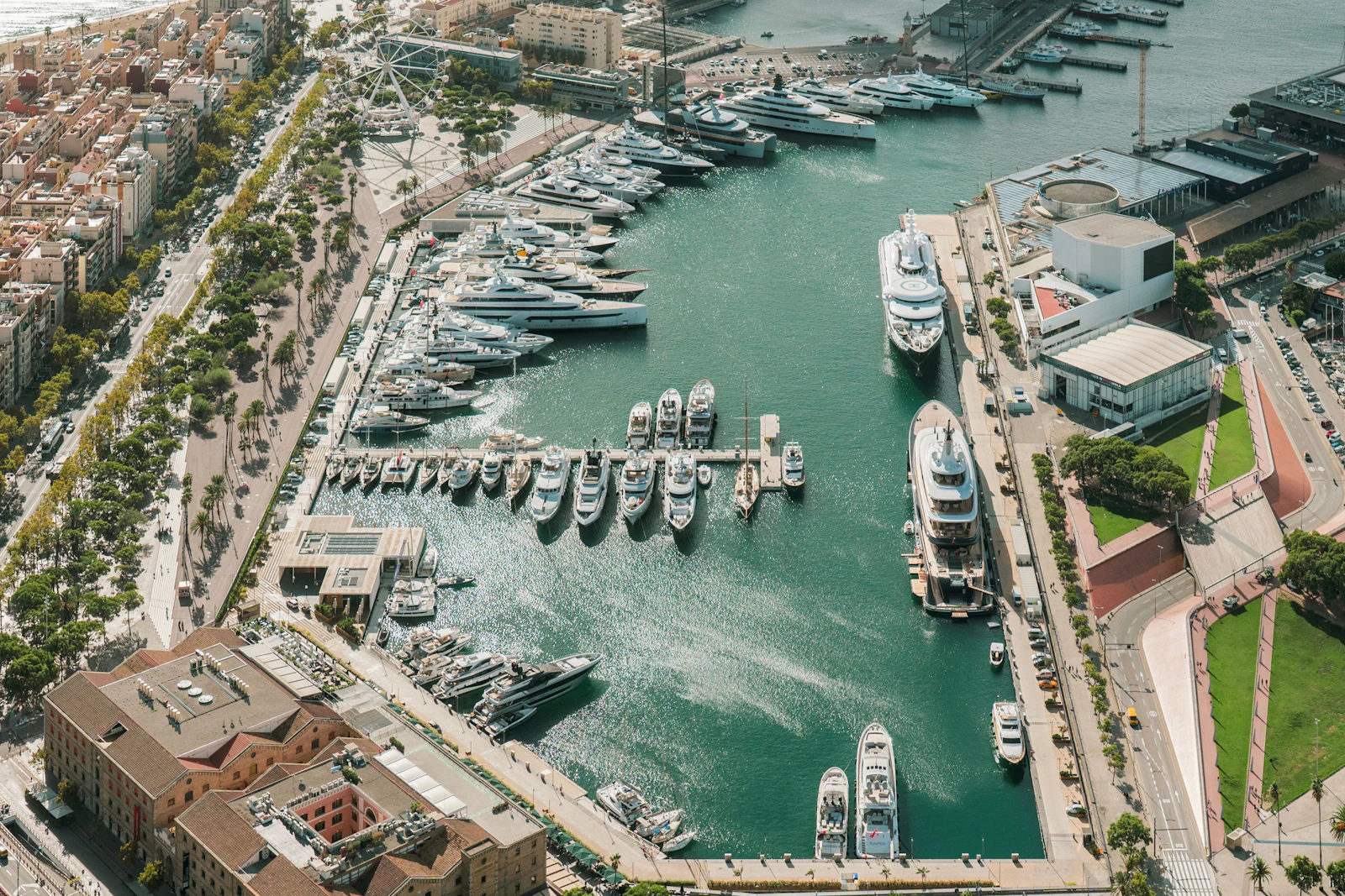 Vista aérea de Marina Port Vell con varios superyates atracados a lo largo del paseo marítimo turquesa en Barcelona.