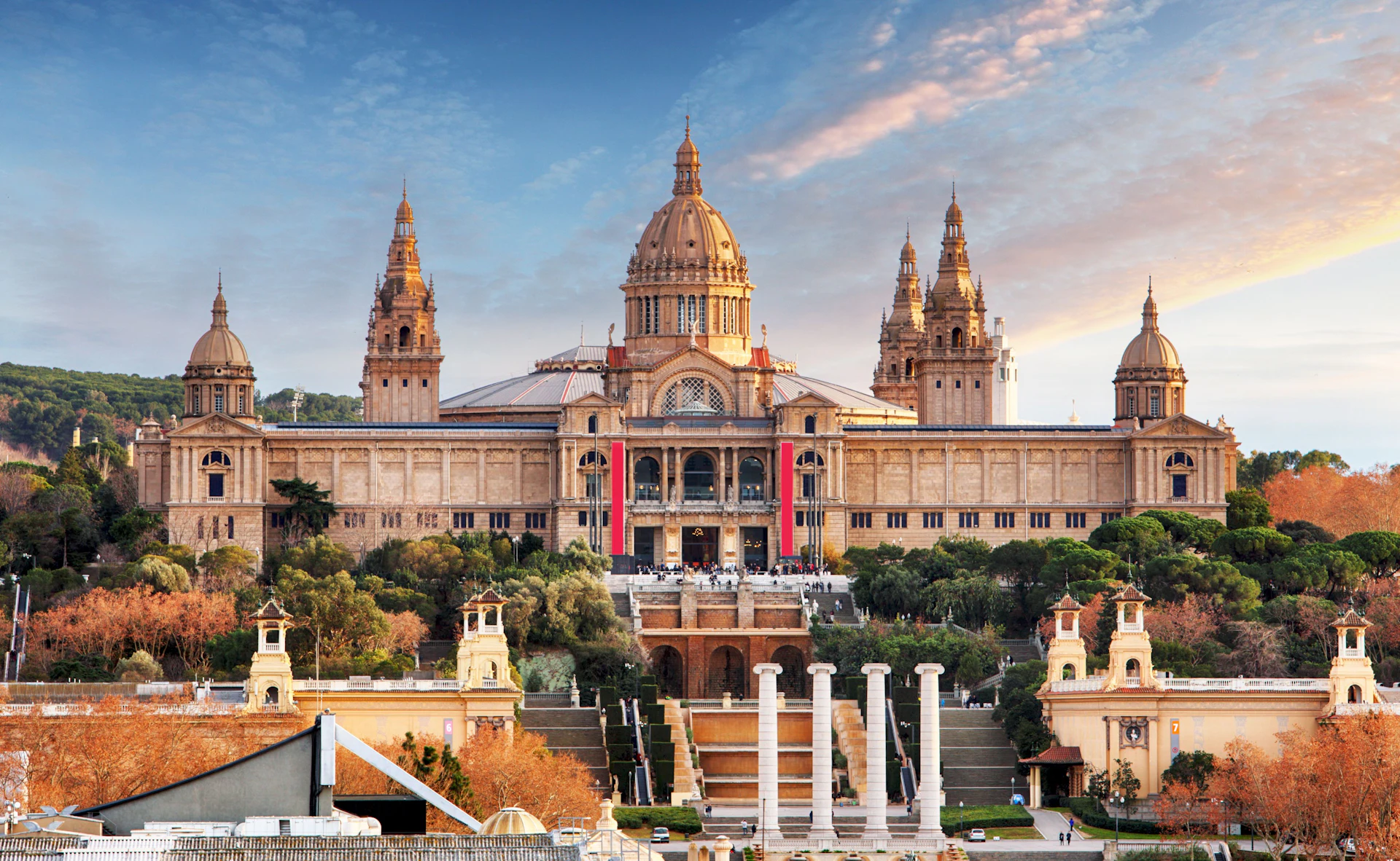 Ornate historic building with golden domes and red banner overlooking waterfront plaza with columns.