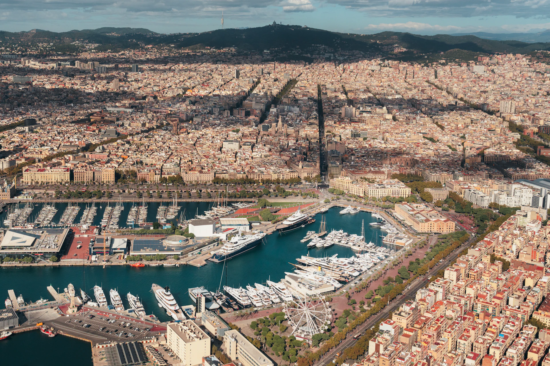 Aerial view of Barcelona's waterfront with Marina Port Vell and moored superyachts surrounded by the city.