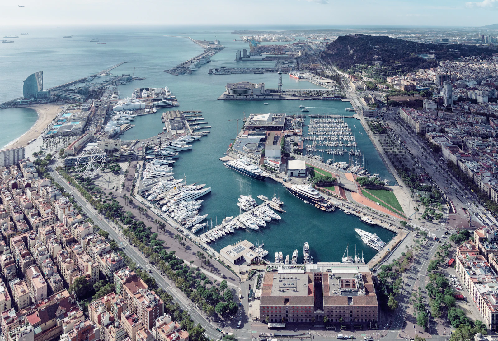 Aerial view of Barcelona's Port Vell marina with numerous superyachts moored in turquoise water.