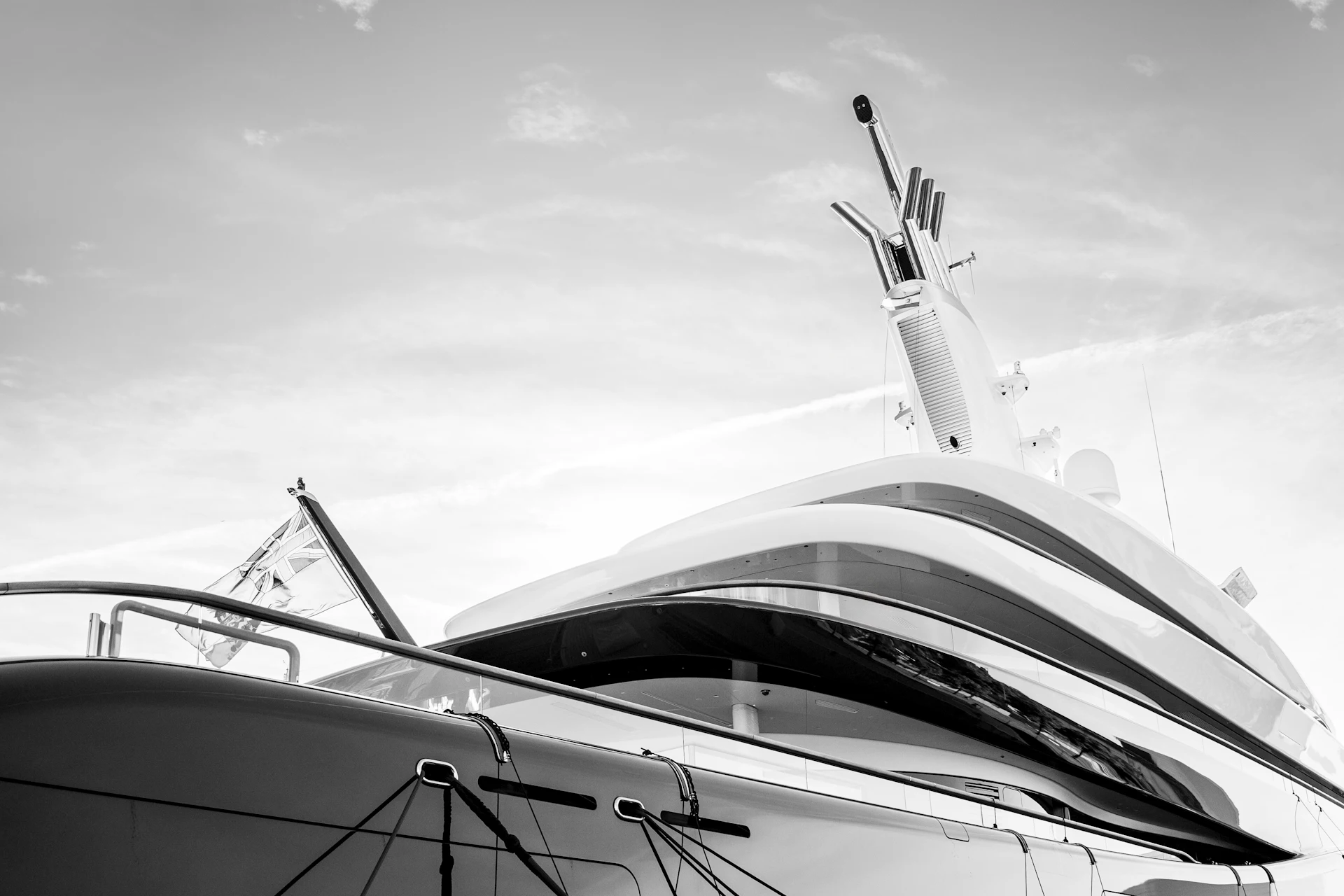 White superyacht with radar mast and antennas moored at marina under cloudy sky.