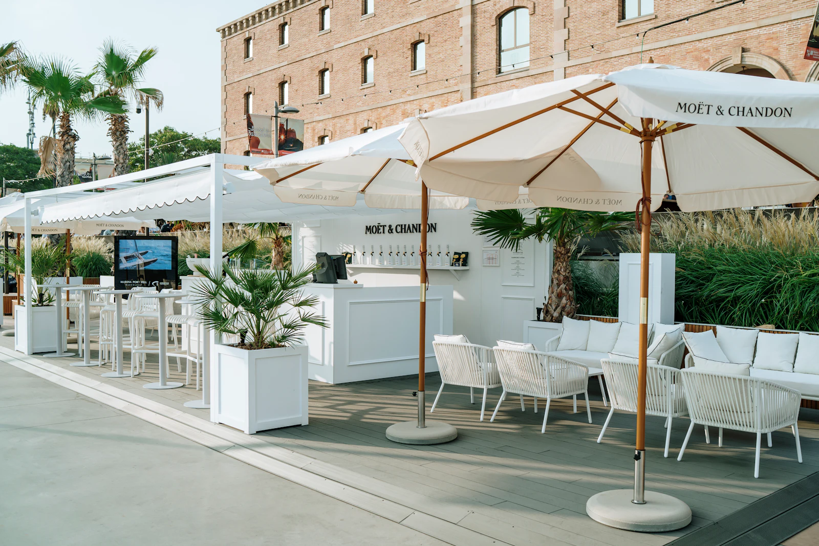 Terraza exterior con sombrillas blancas, zonas de descanso y un bar de la marca Moët & Chandon junto a un edificio histórico de ladrillo.