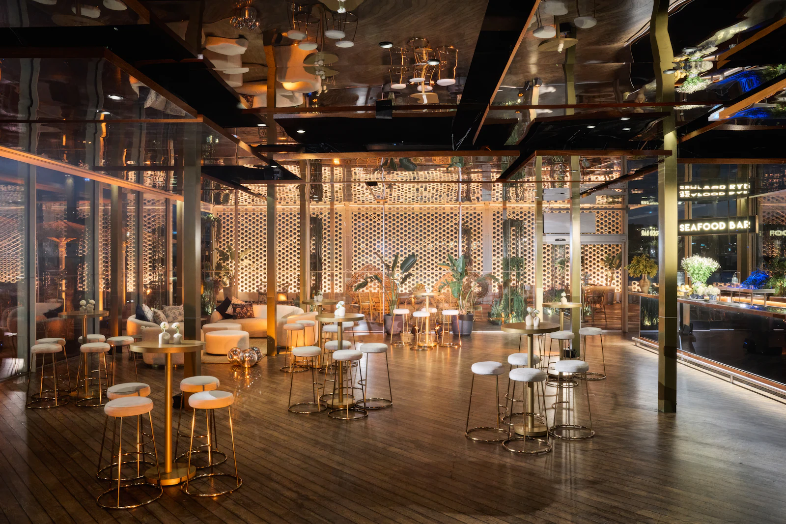 Modern seafood bar interior with orange and white bar stools, geometric lattice walls, and waterfront views at night.