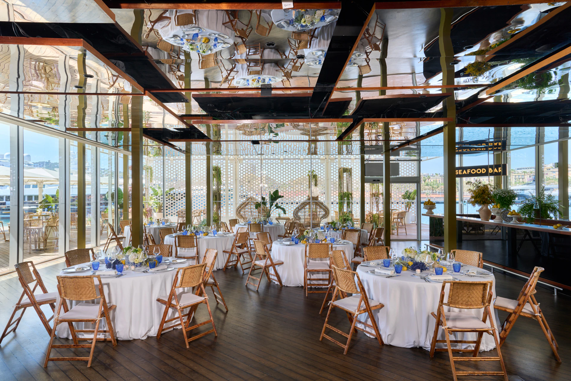 Elegant event space with round tables, wooden chairs, and blue accents overlooking Barcelona marina.