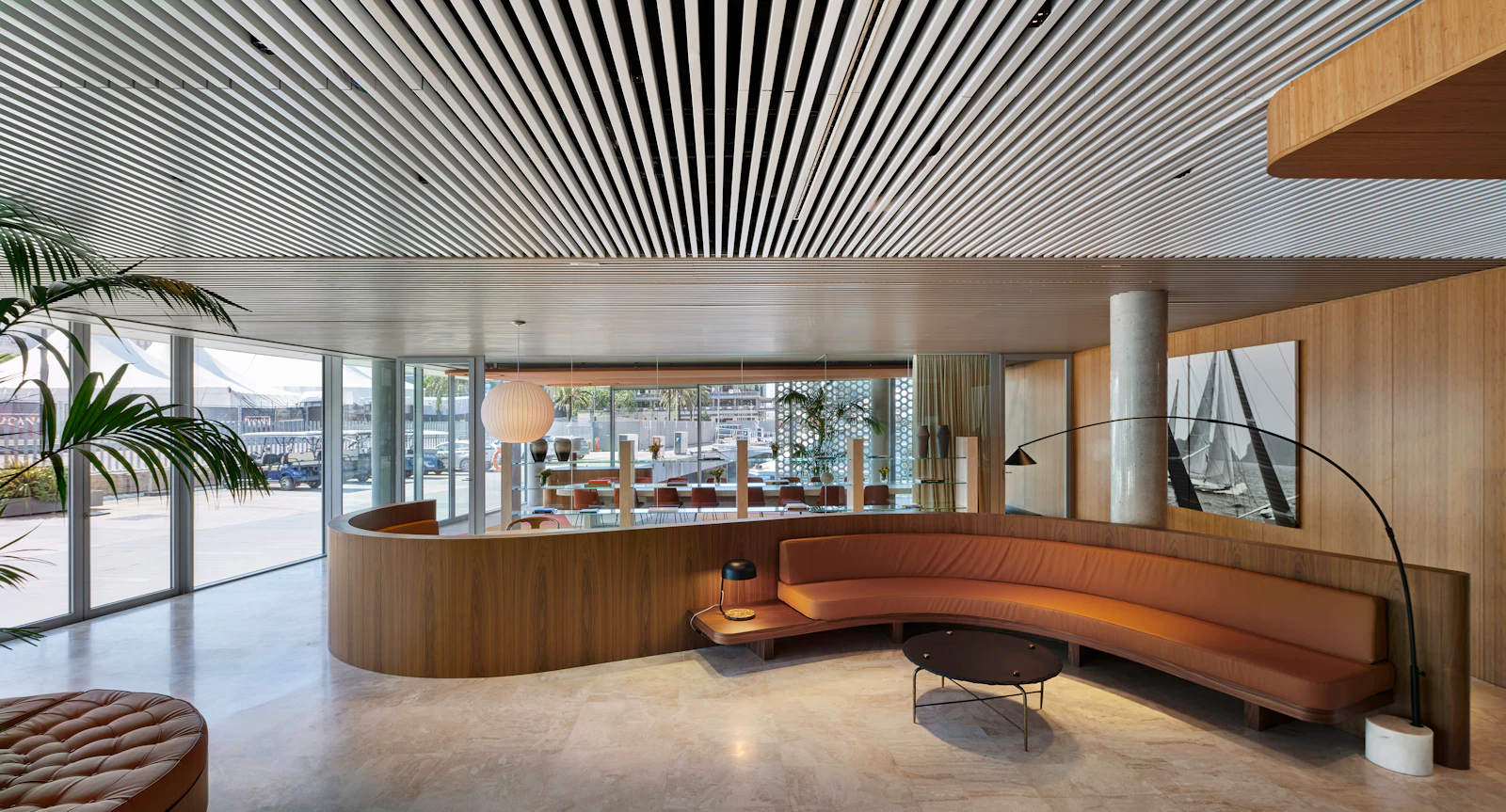 Salón moderno con sofá curvo de piel, revestimiento de madera y vistas al puerto a través de paredes de cristal.