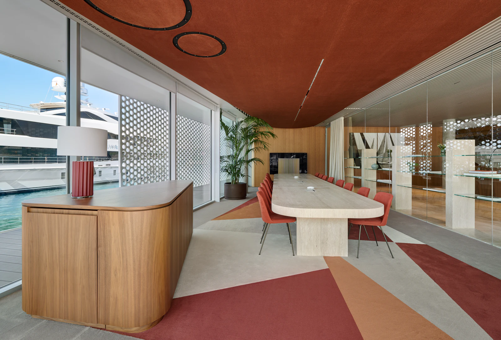 Sala de reuniones moderna con mesa larga y sillas rojas con vistas a un yate amarrado.