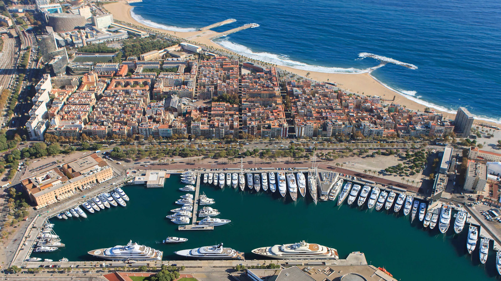 Aerial view of Marina Port Vell showing multiple superyachts moored in Barcelona's waterfront basin.