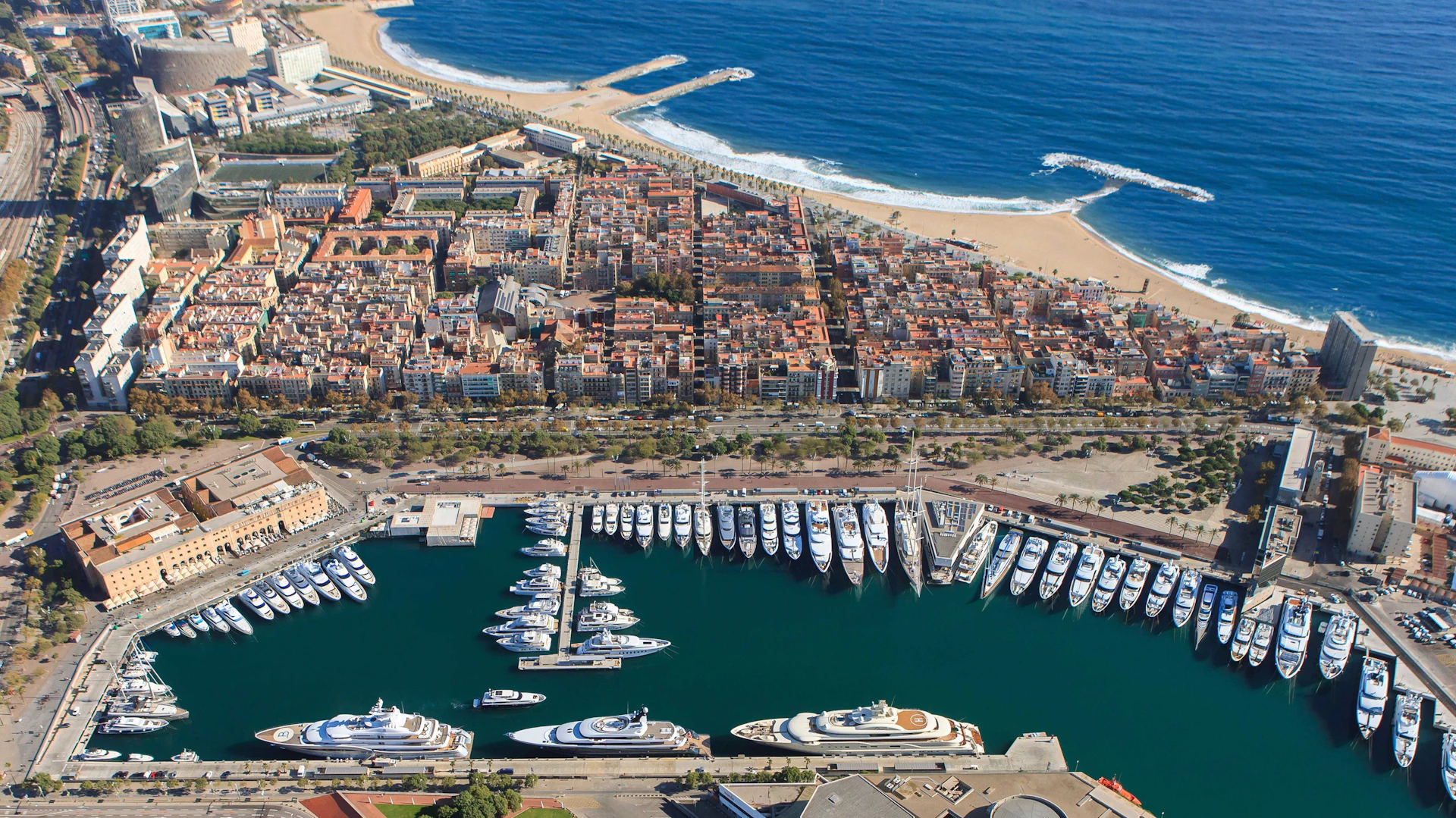 Aerial view of Marina Port Vell showing multiple superyachts moored in Barcelona's waterfront basin.