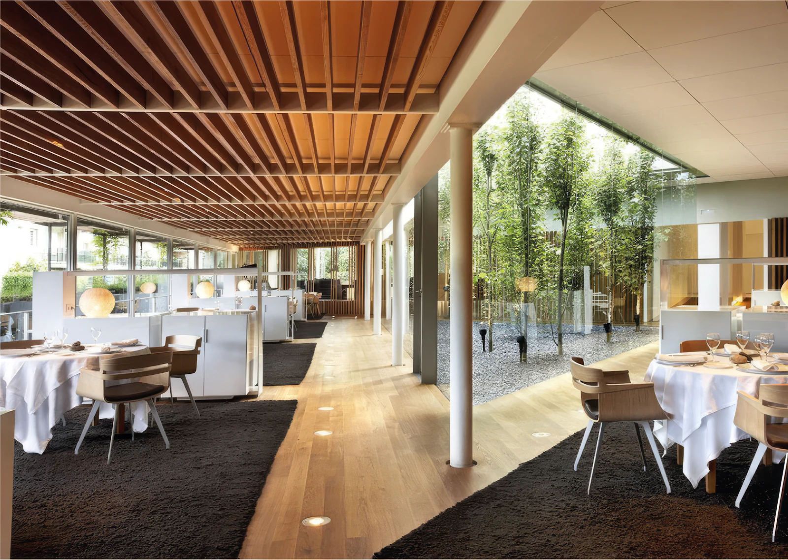 Restaurant dining room with wooden slat ceiling and tables beside a bamboo courtyard.