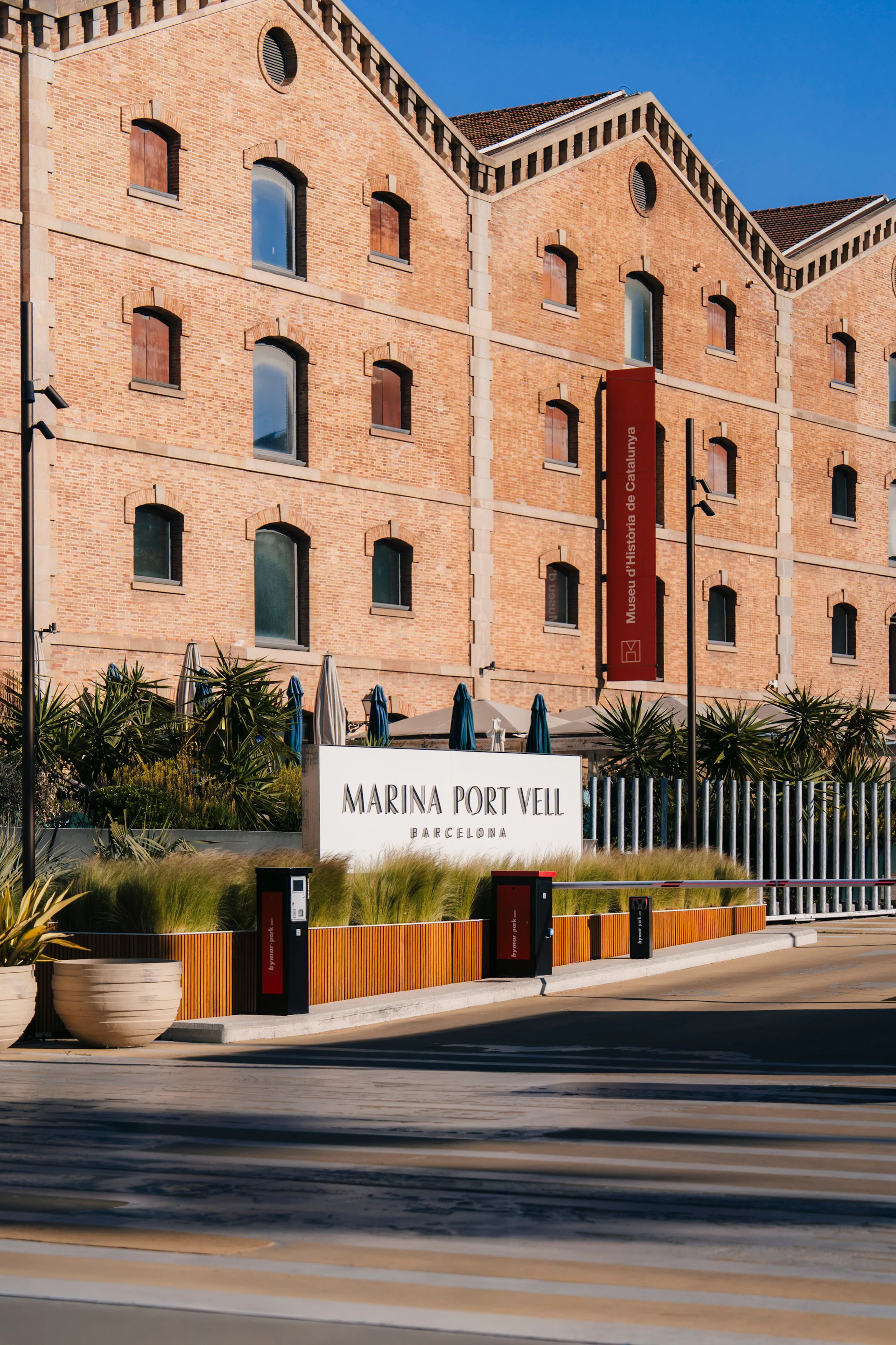 Edificio histórico de ladrillo con el rótulo de Marina Port Vell Barcelona y entrada frente al mar.