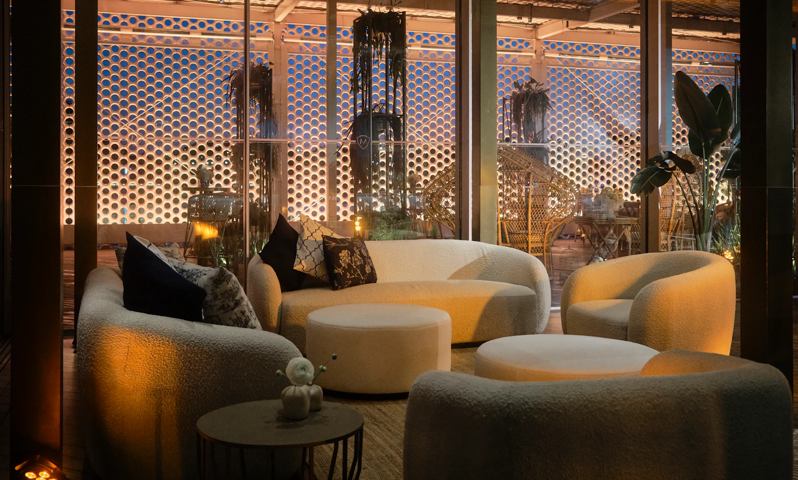 Cosy lounge with cream boucle sofas and ottomans against a lit perforated wall.