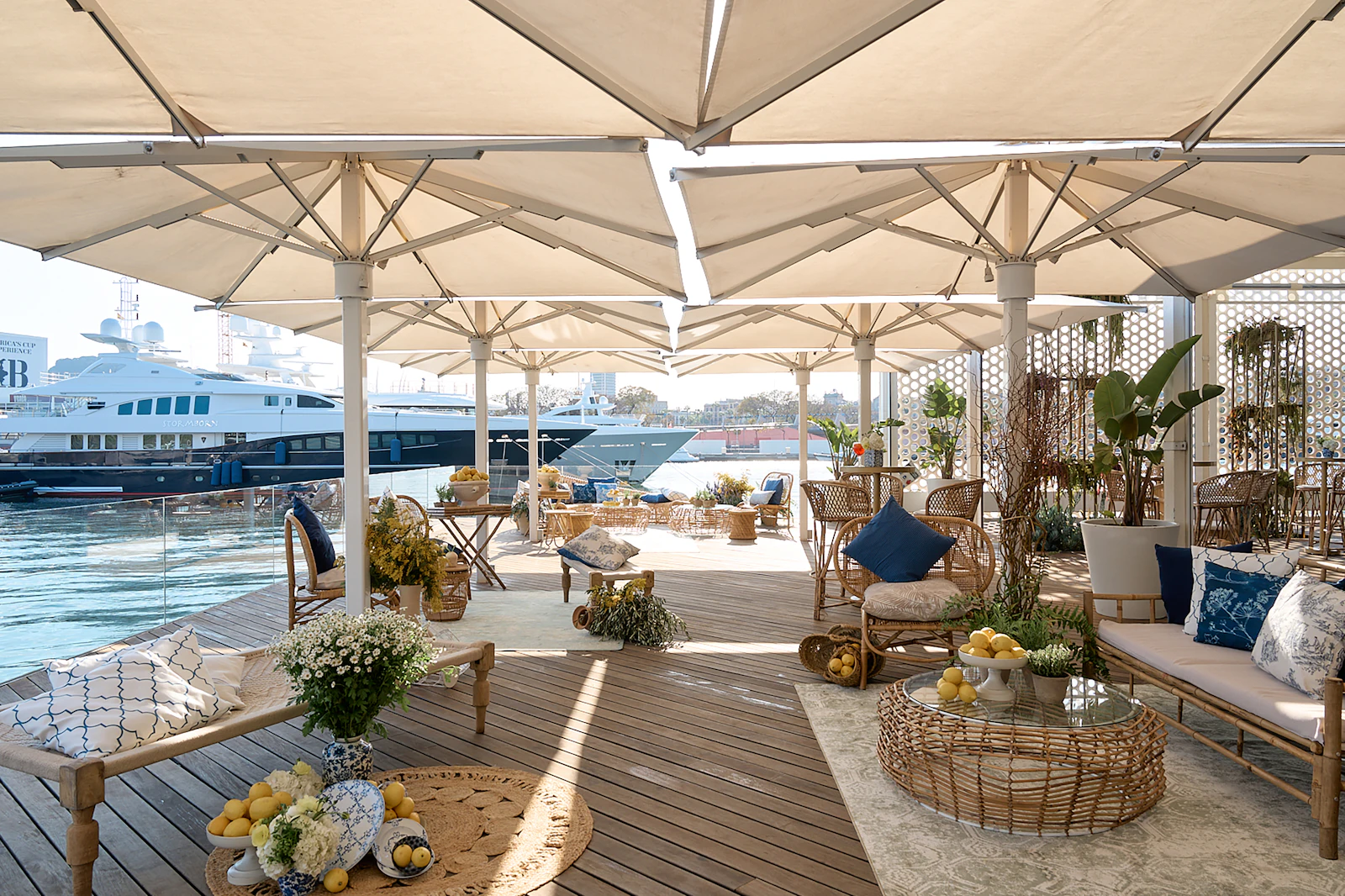 Waterfront terrace with umbrellas, rattan furniture and lemons, overlooking moored superyachts.
