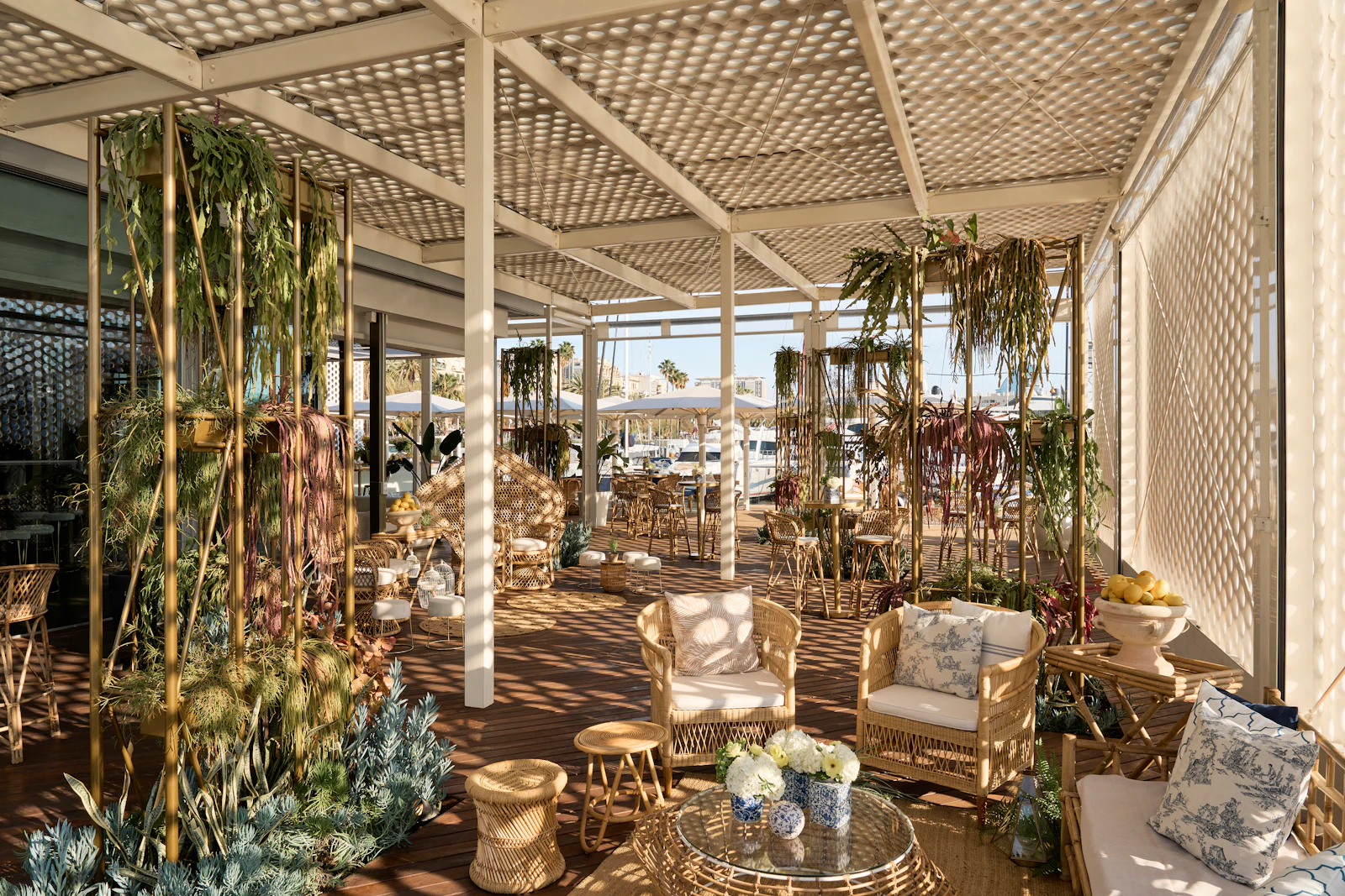 Covered terrace lounge with rattan furniture, hanging plants, and marina views in the background.