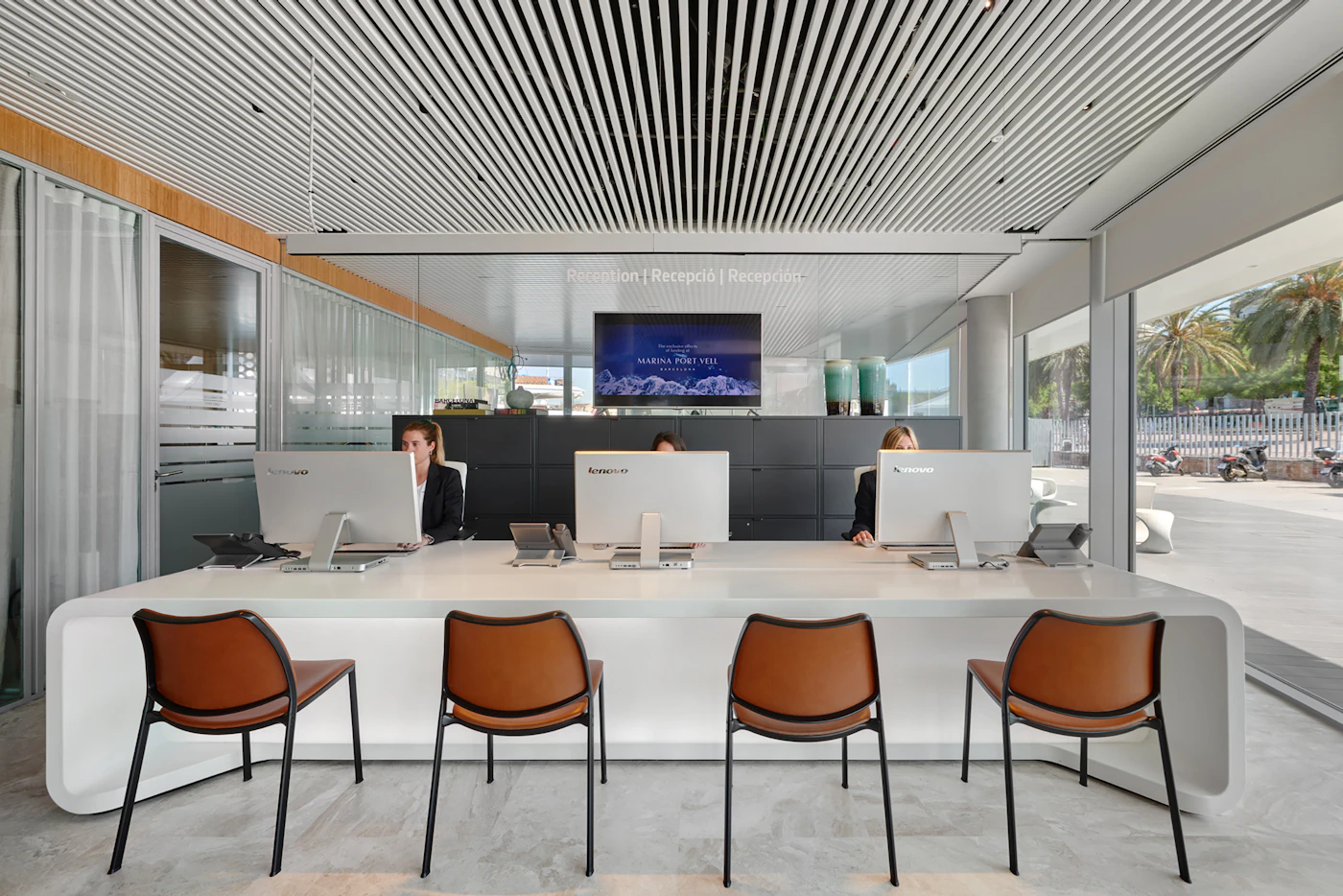 Three staff work at computers behind a white reception desk with leather chairs.