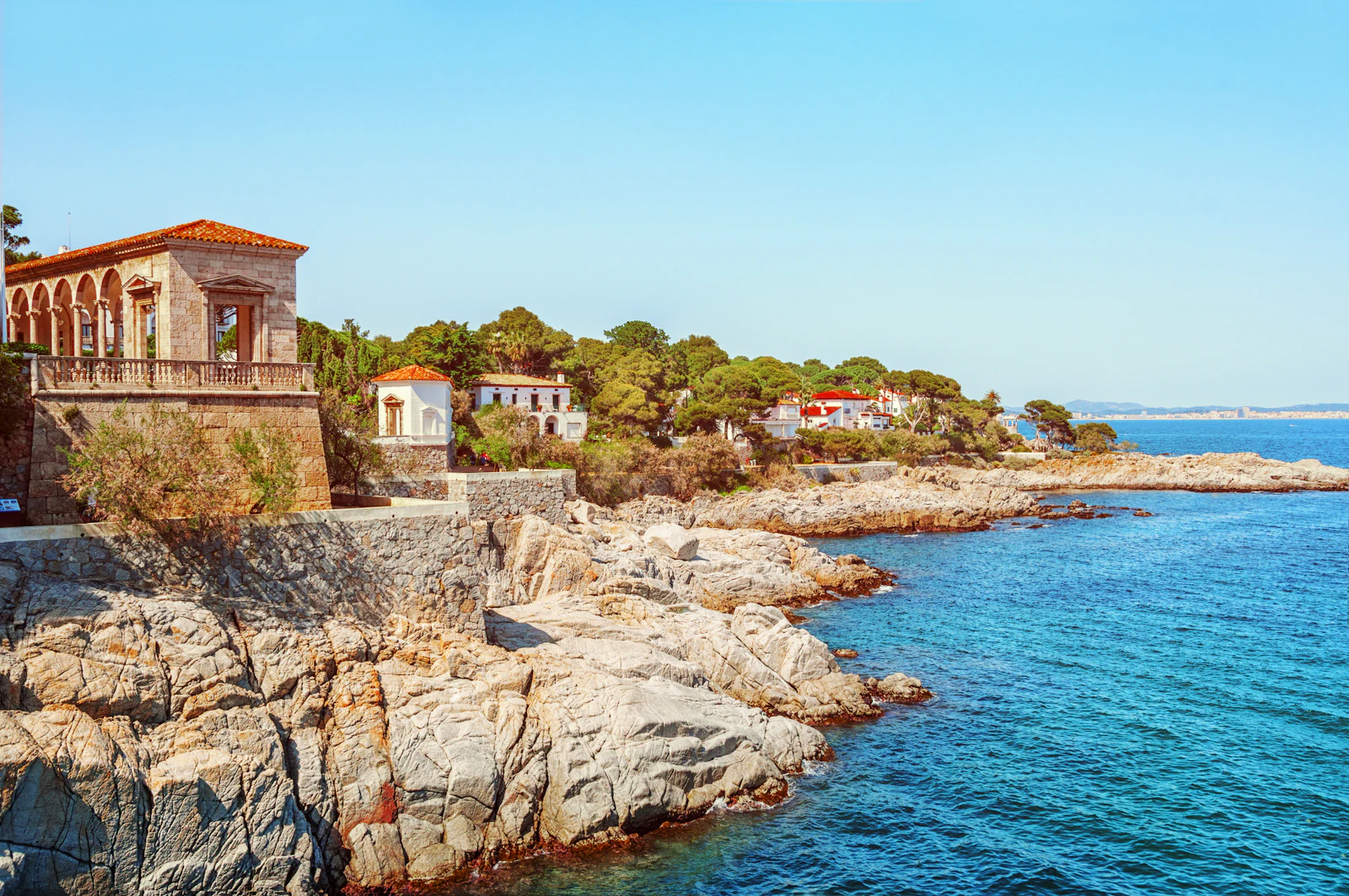 Rocky coastline with villas and a stone terrace overlooking the blue sea.