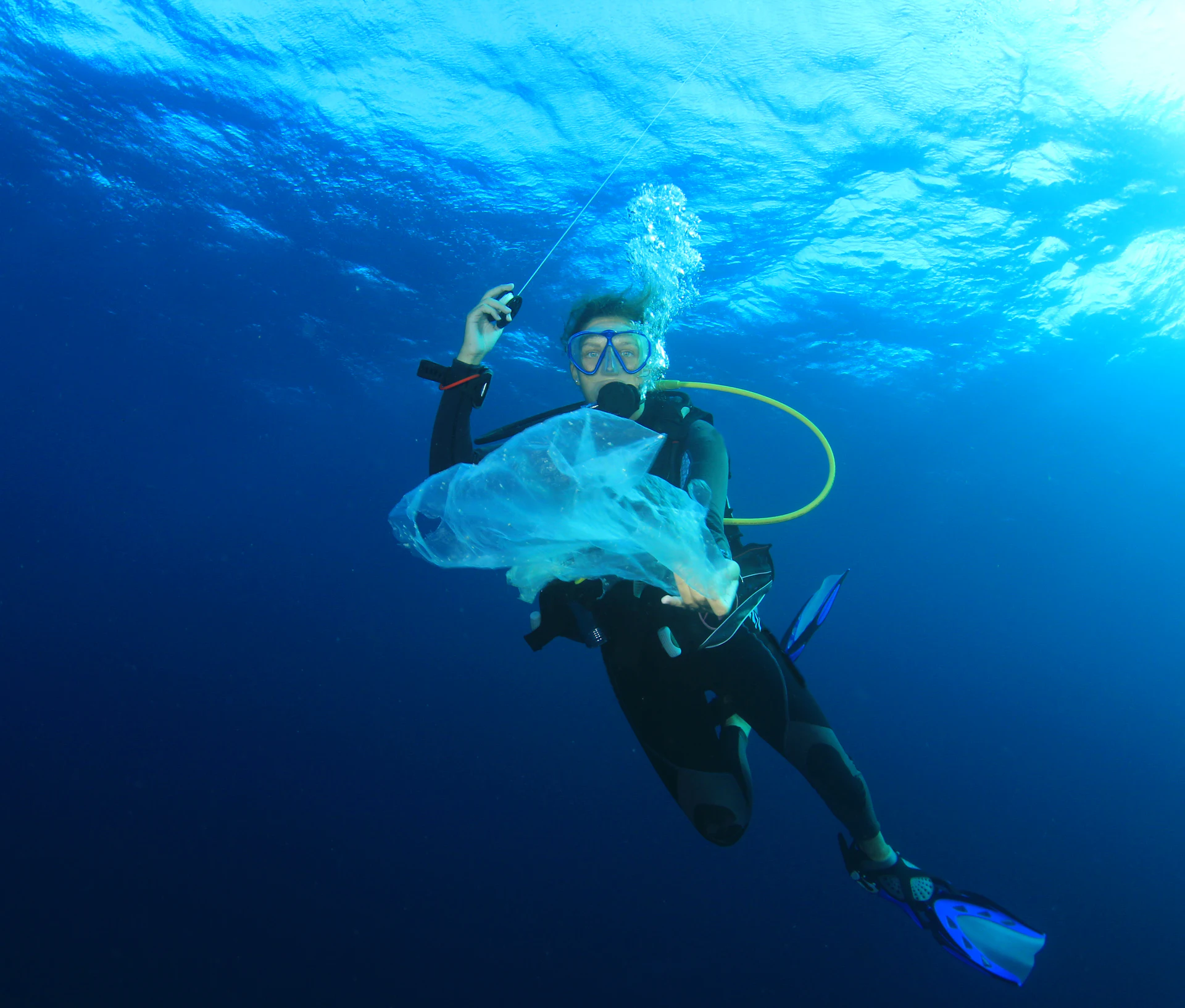 Scuba diver underwater holding a piece of plastic debris while looking at the camera.