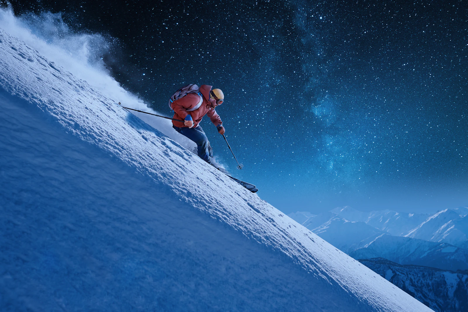Skier in red jacket descending a snowy slope under a starry night sky.
