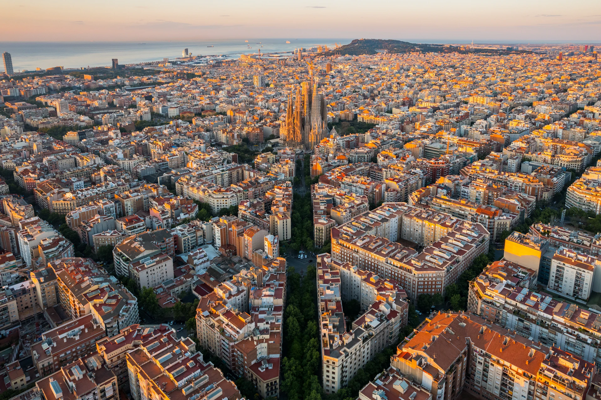 Aerial view of Barcelona's grid streets with the Sagrada Família and sea at sunset.
