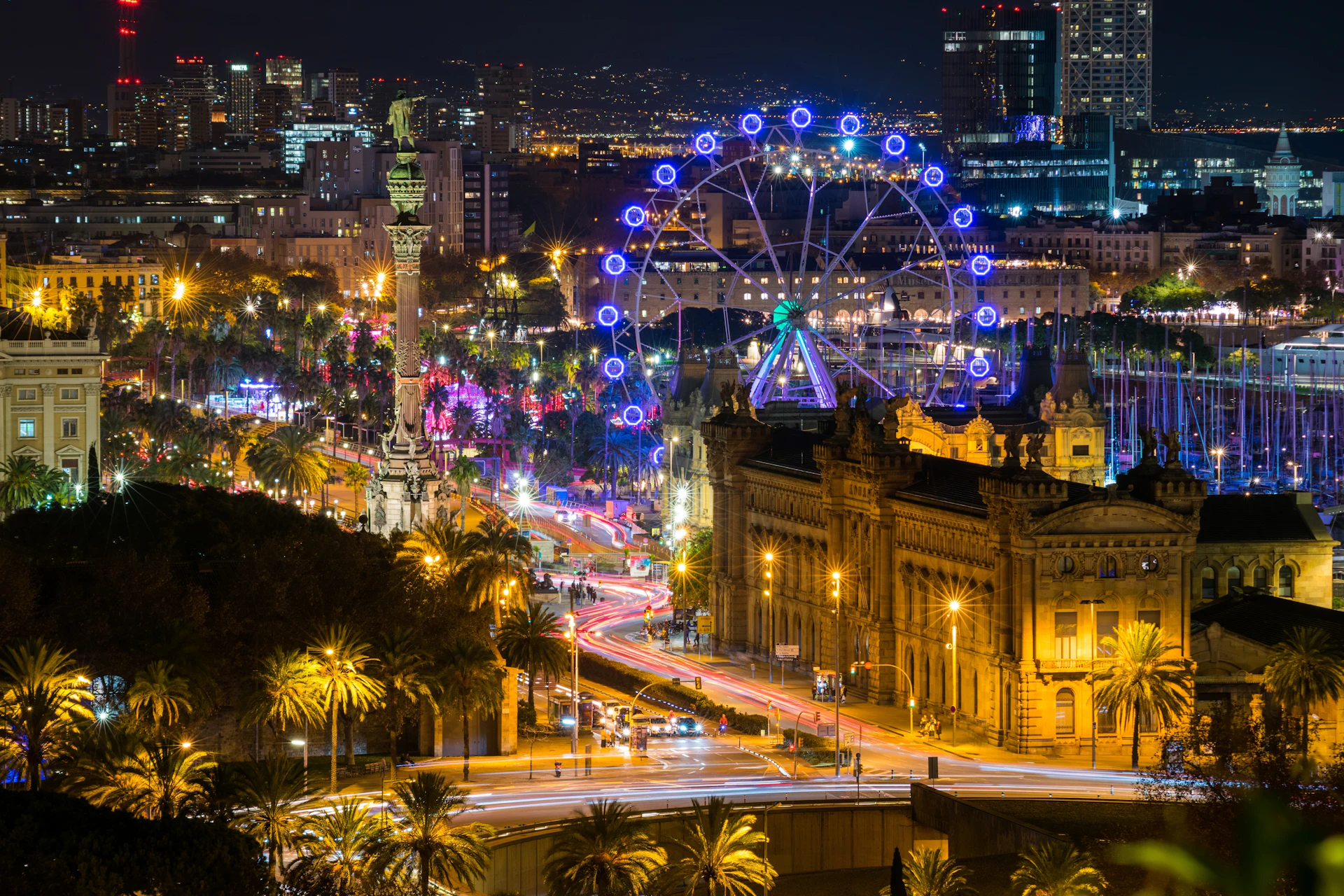 Barcelona at night with an illuminated Ferris wheel, Columbus monument and traffic light trails.