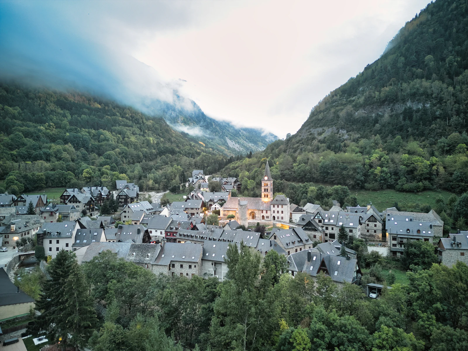 Mountain village with a stone church tower nestled in a misty forested valley.
