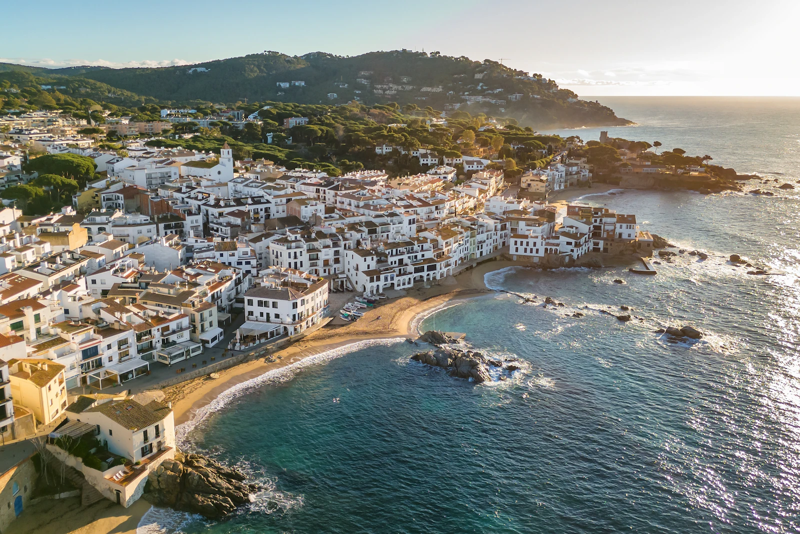 Aerial view of a whitewashed coastal town with sandy beaches and rocky shoreline.