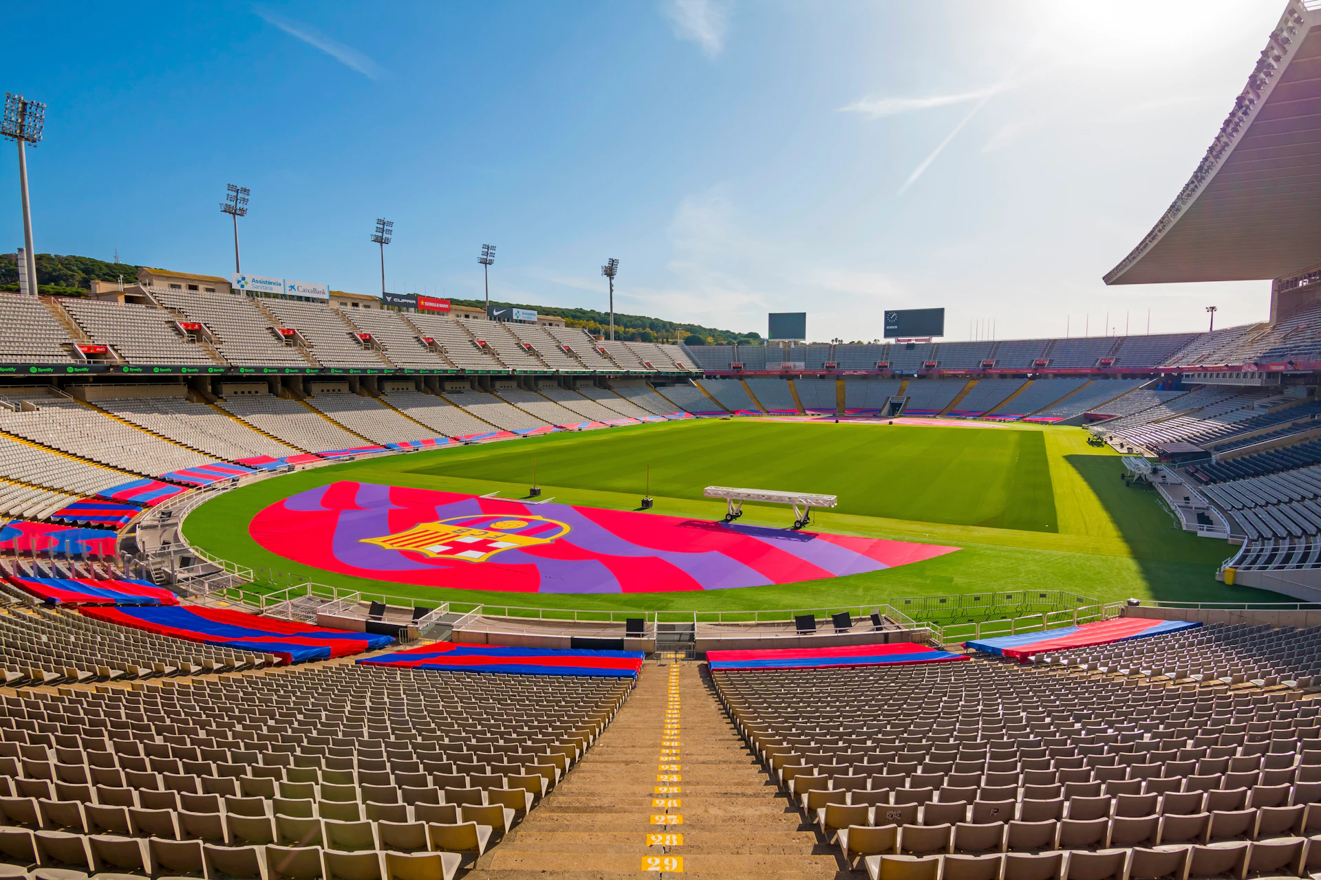 Large football stadium with red and blue seats displaying a team crest on the pitch.