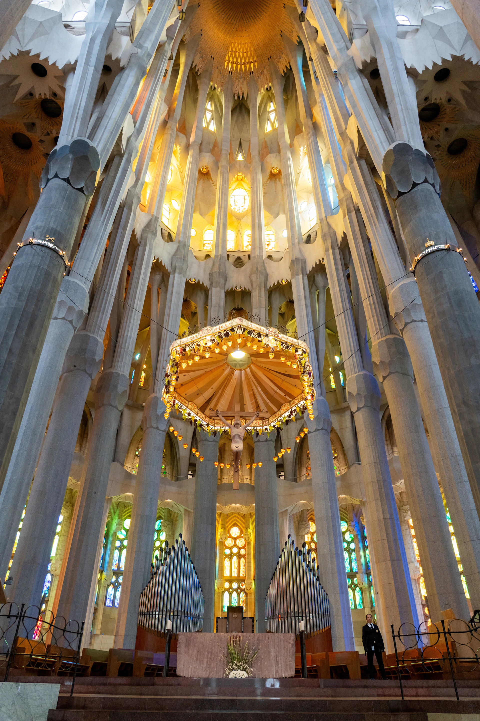 Interior of Sagrada Família basilica showing soaring columns, stained glass windows, and illuminated chandelier.