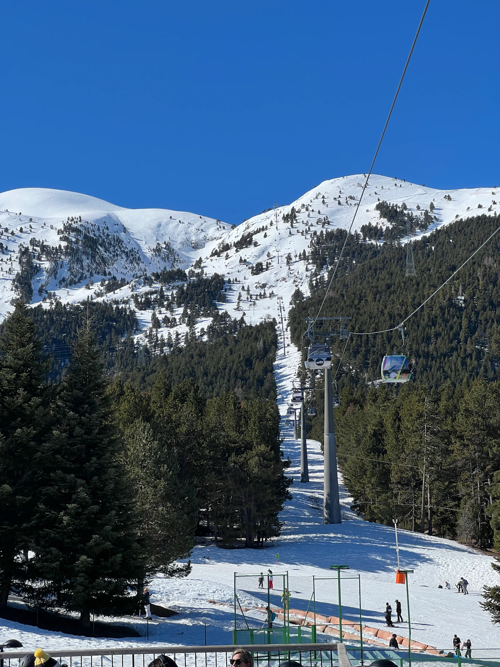 Gondola cable cars ascending a snow-covered mountain ski resort under clear blue sky.