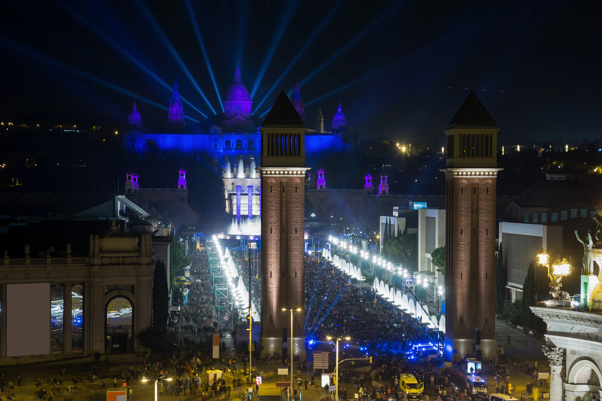 Nighttime view of Barcelona's Plaça Reial with illuminated twin towers and blue-lit buildings during an event.