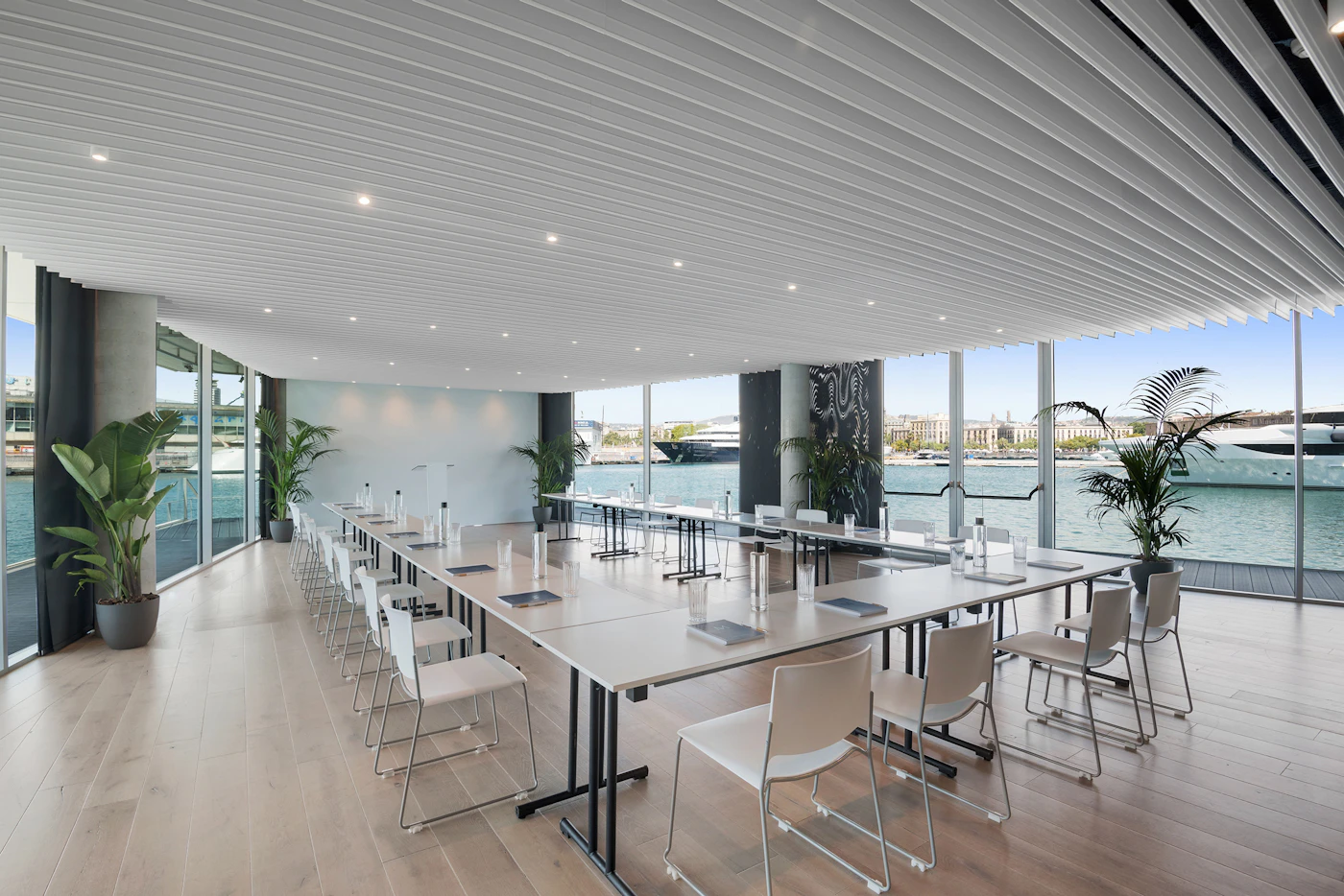 Long meeting room with white tables and chairs overlooking the marina and yachts.