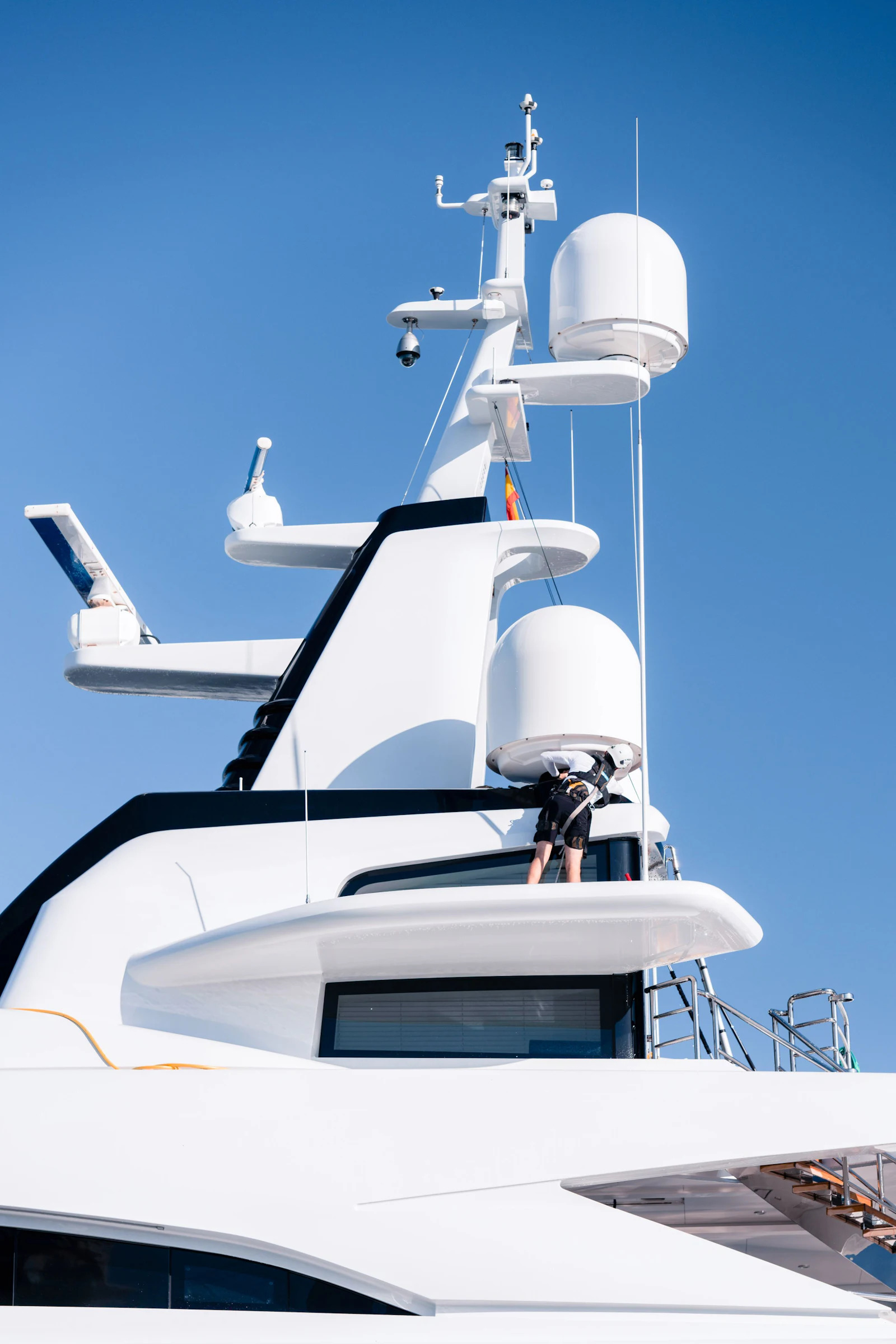 White superyacht with communication masts and radar domes against a clear blue sky.