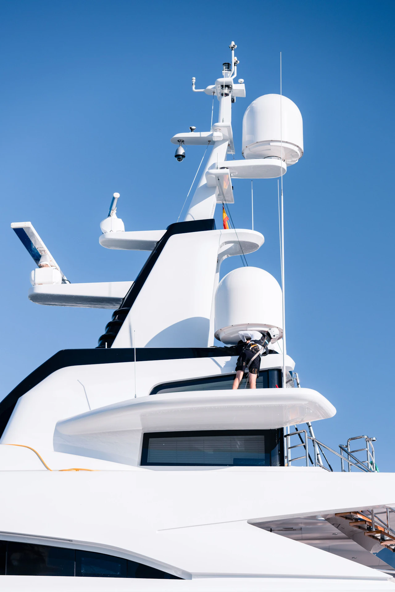 White superyacht with communication masts and radar domes against a clear blue sky.