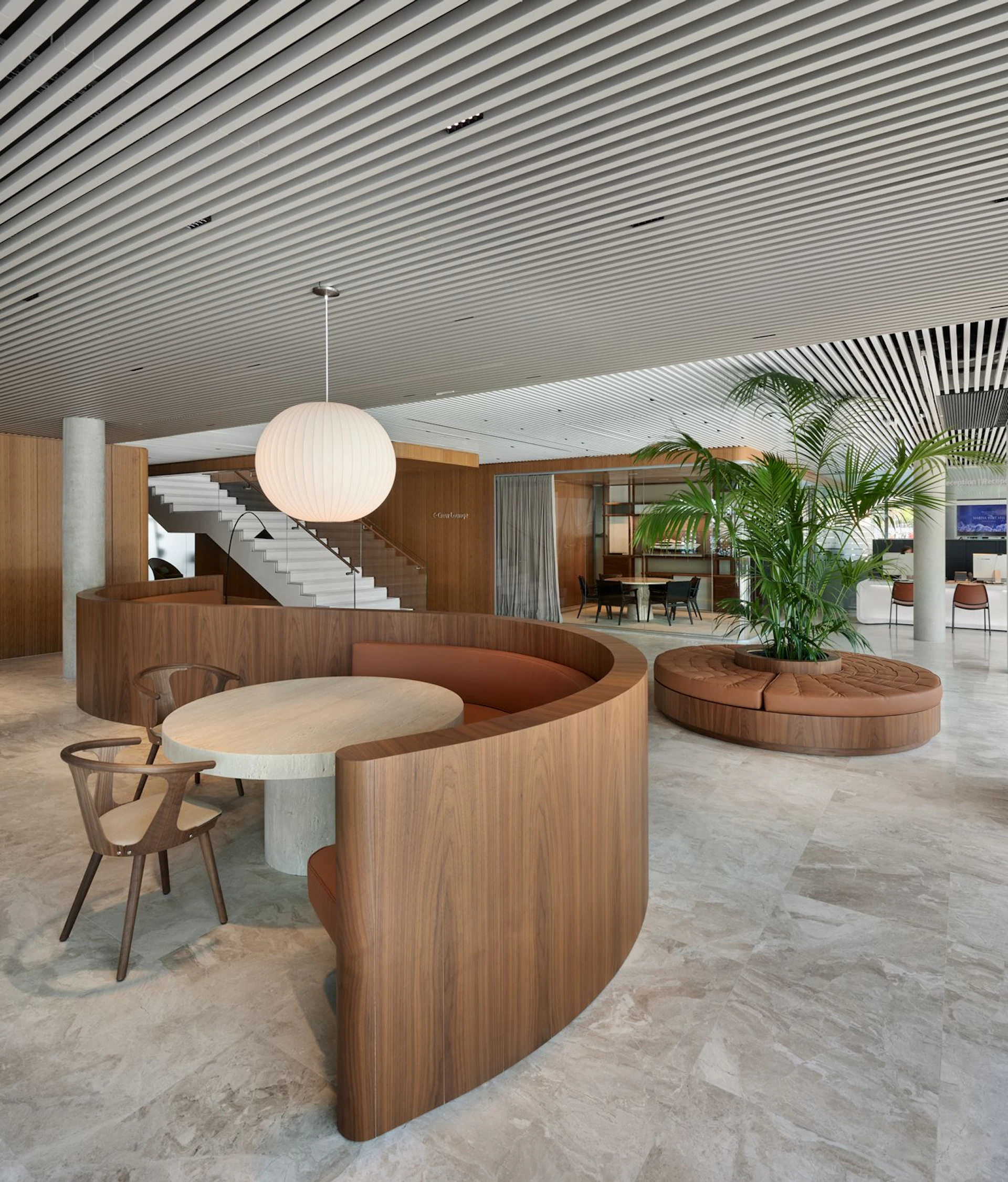 Salón interior moderno con muebles de madera curvados, lámparas colgantes y plantas tropicales bajo un techo de rayas.