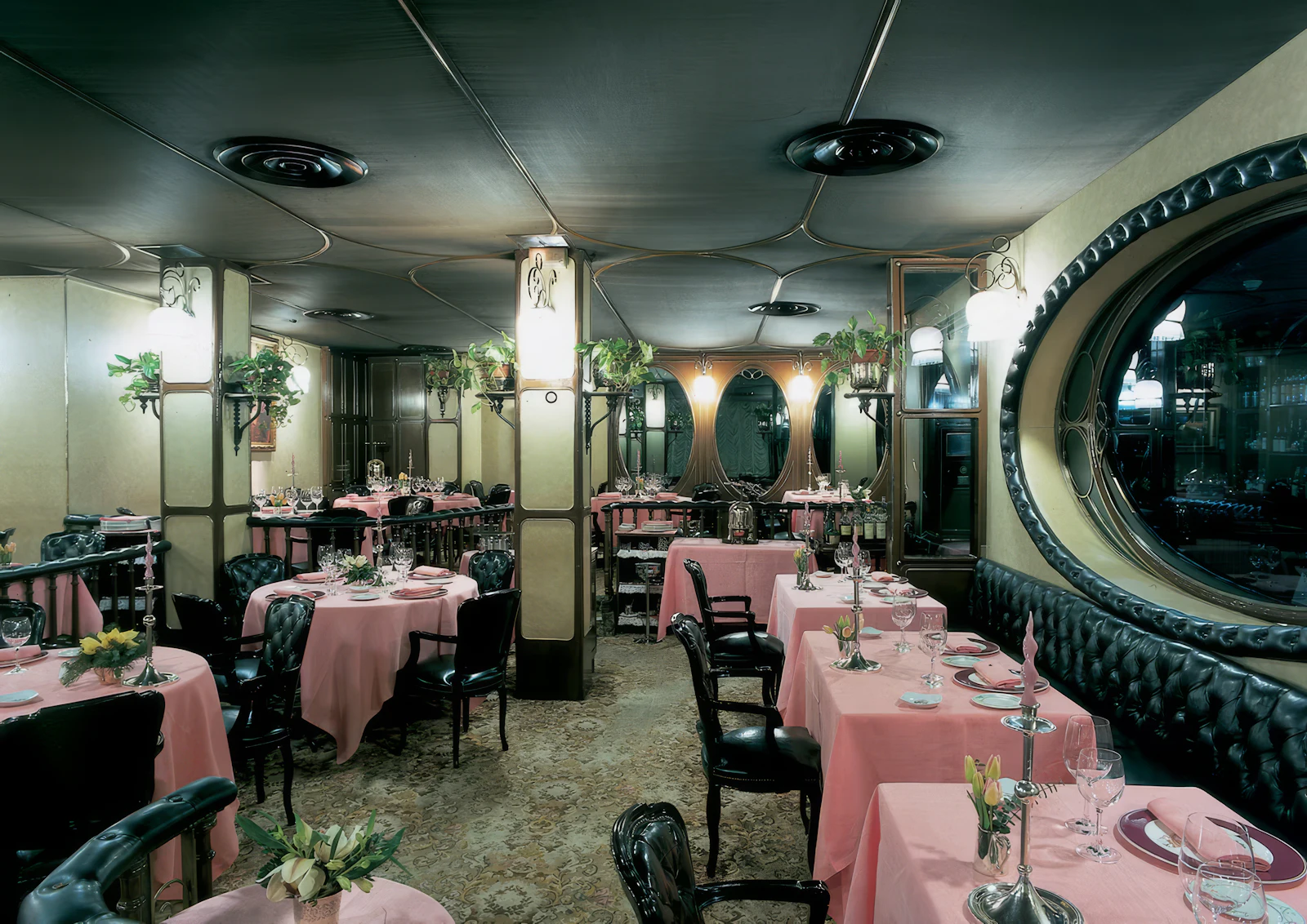 Elegant restaurant interior with pink-clothed tables, black leather seating and Art Nouveau décor.
